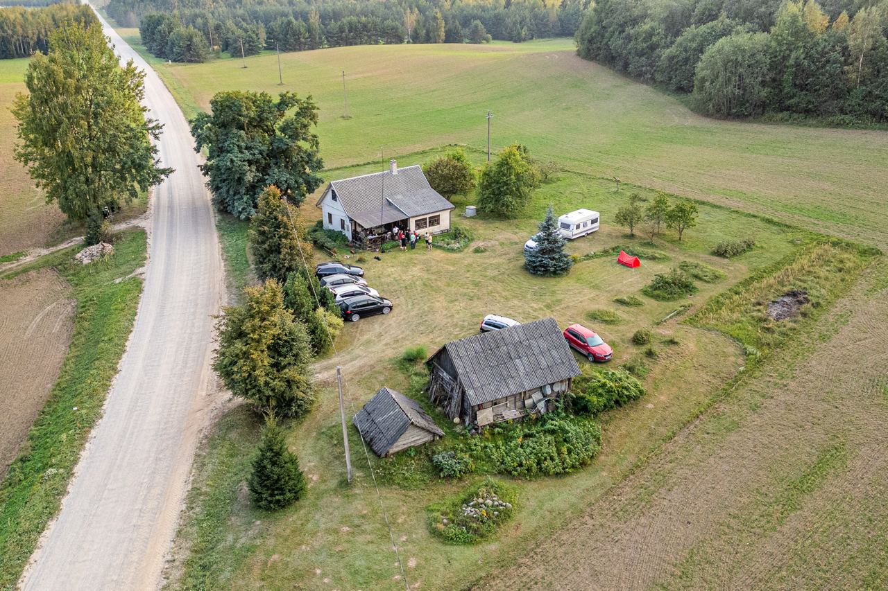 VU radijo klubo sąskrydis iš oro, sodyba, šalia jos antenos stiebas. Prie sodybos būrys žmonių. Didelis kiemas, jame stovi mašinos, palapinė, kemperis. Aplink laukai, miškas, šalia žvyrkelis.